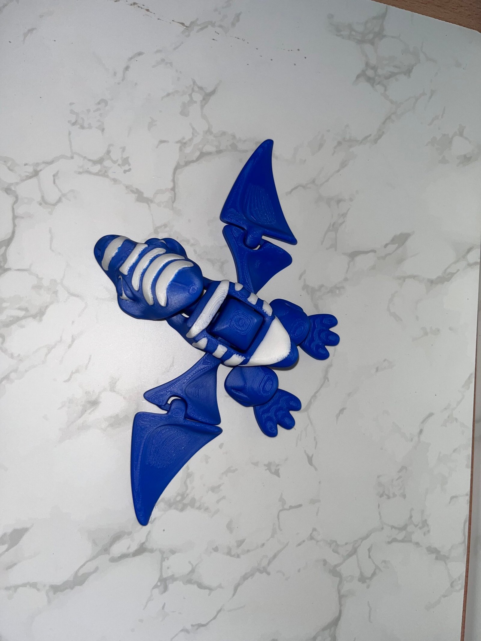 IMG_1403 AUTO-DRAFT: Blue and white 3D-printed articulated pterodactyl toy, showcasing flexible design.
